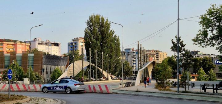 A police car parked near a construction barrier at a city intersection, surrounded by trees and modern buildings.