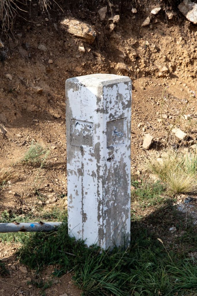 A weathered concrete boundary marker with two compartments, situated on a dirt path surrounded by grass and rocks.