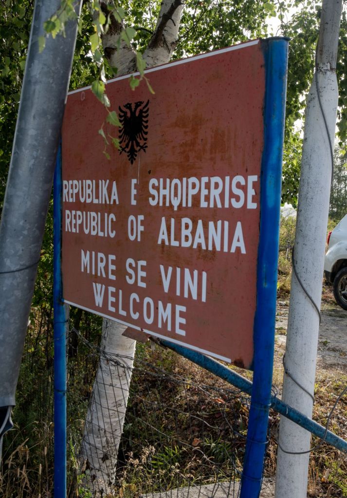 Sign welcoming visitors to the Republic of Albania, displaying text in Albanian and English.