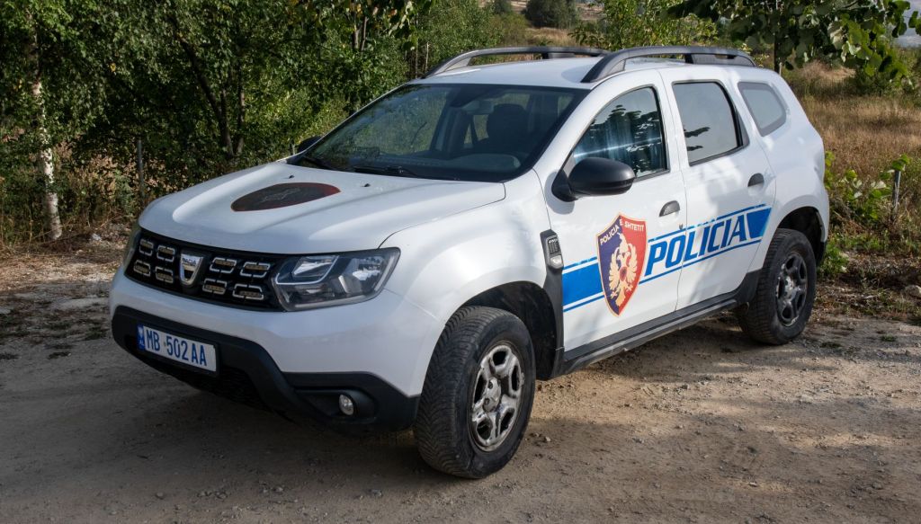 A white police vehicle parked on a dirt road surrounded by greenery.