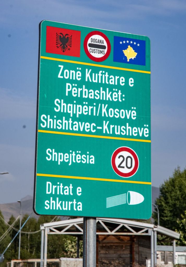 Traffic sign indicating the border zone between Albania and Kosovo, featuring flags of both countries, customs information, and speed limit of 20 km/h.