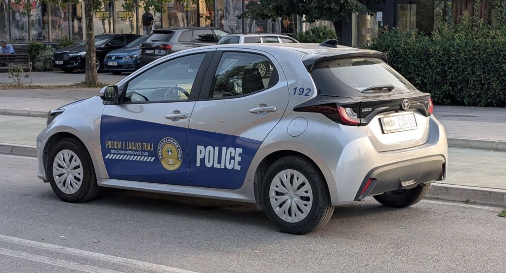 A silver police car parked on a street, displaying the word 'POLICE' and markings in blue. The vehicle is a Toyota Yaris and has a visible police badge on the side.