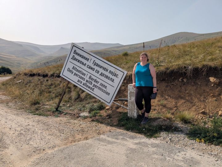 A person standing beside a large sign warning of a border zone, written in multiple languages, indicating that only authorized individuals are allowed.